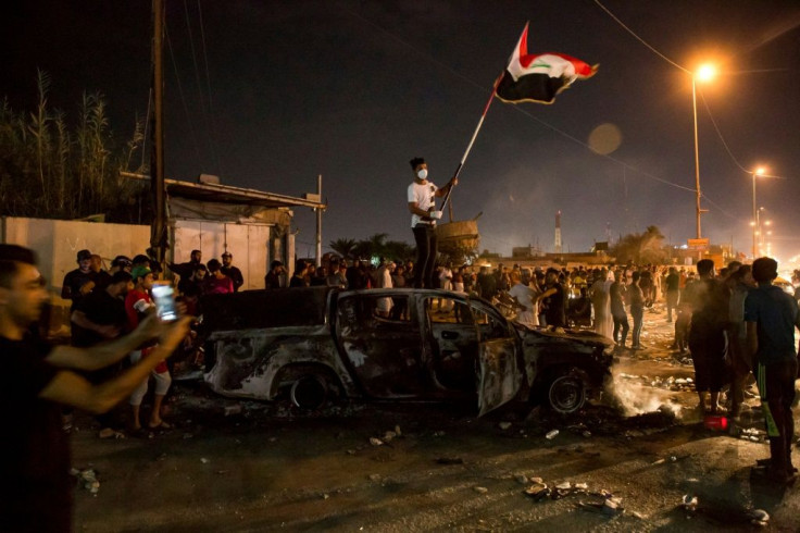 An Iraqi protester waves the national flag as he stands atop a burnt out police vehicle outside the local government headquarters in the southern city of Basra on Friday