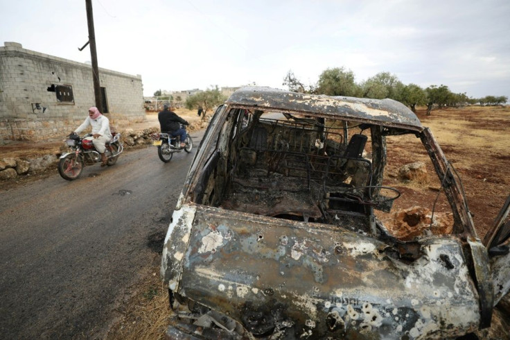 Bikers ride past a damaged car at the site of a suspected US-led operation against Islamic State chief Abu Bakr al-Baghdadi in the Syrian village of Barisha