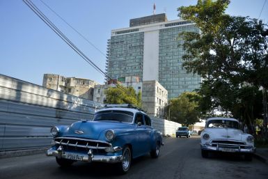 Old American cars drive near the Habana Libre Hotel in February 2019