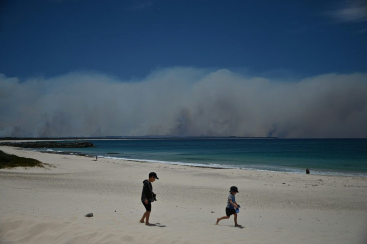 Bushfires burn in the distance as children play on a beach in Forster, north of Sydney