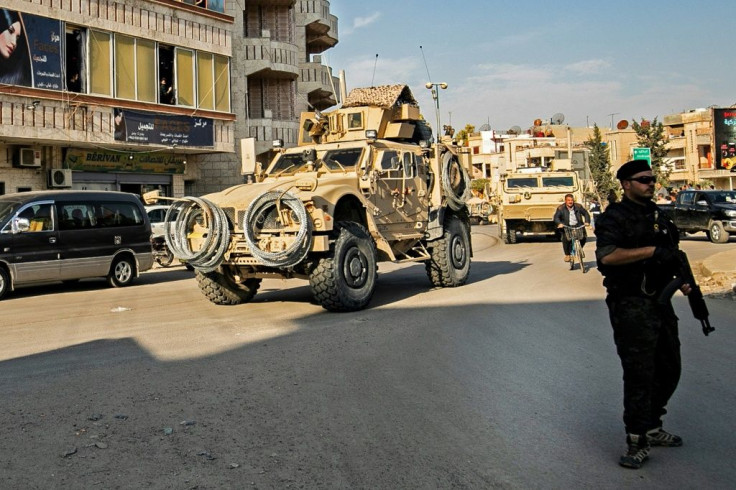 A member of the Syrian Democratic Forces stands on the side of a road as US military vehicles drive east of the Kurdish-controlled northeastern Syrian city of Qamishli