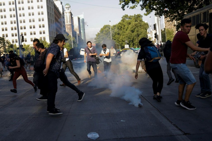 Demonstrators run away from tear gas during clashes with riot police following a mass fare-dodging protest in downtown Santiago, on October 18, 2019