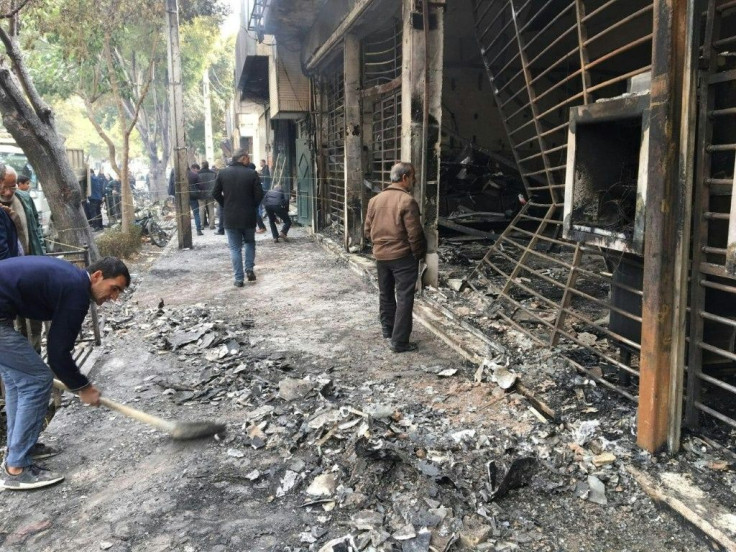 Iranians walk past the charred remains of a bank branch that was set ablaze by protesters in the central city of Isfahan