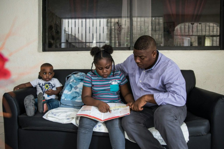 Samy Janvier (R) teaches his eight-year-old daughter Samara at home, while her two-year-old brother Samy Jr watches