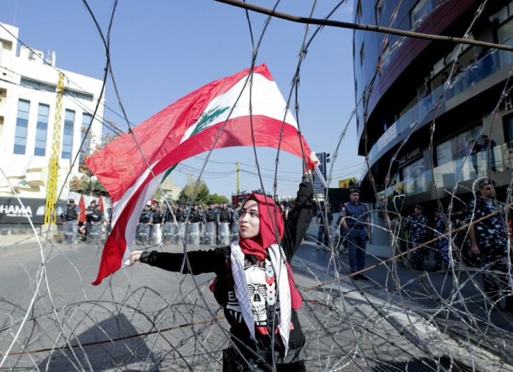 A Lebanese demonstrator waves the national flag while security forces stand by