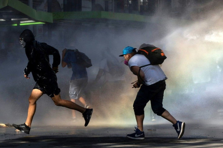 Demonstrators run from a water cannon during a protest against the government in Santiago