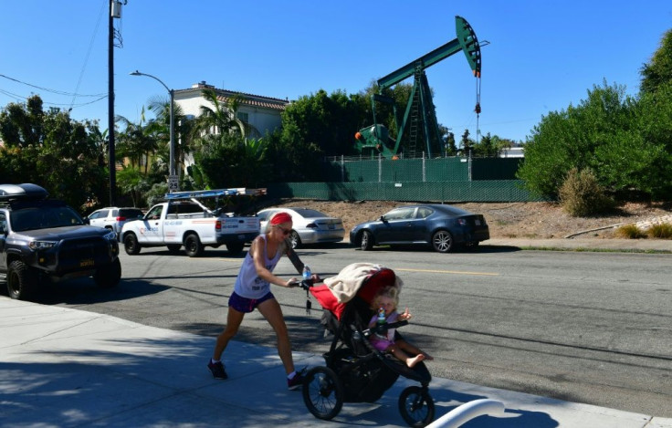 Heather Hartmann pushes her daughter Everly, age 2, in a stroller past a pumpjack in an oil well on October 21, 2019 in Signal Hill, which was once called "Porcupine Hill" because of the number of oil derricks that blanketed the area