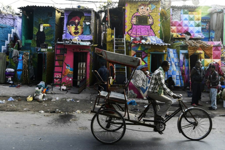 A rickshaw driver cycles past homes adorned with murals by the 'Delhi Street Art' group