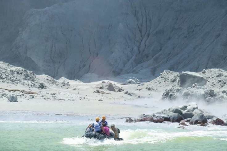 A photo courtesy of Michael Schade shows people being rescued after the White Island volcano erupted - in the background is the wreck of a helicoper