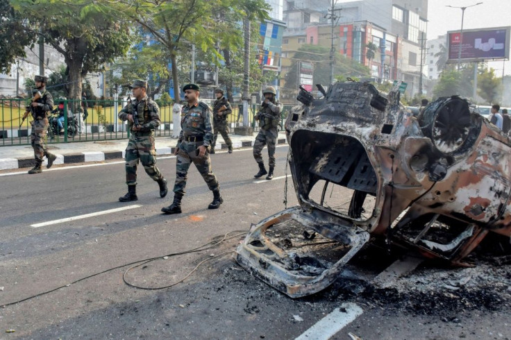 Indian soldiers walk past the burnt wreckage of a vehicle torched by protestors in Guwahati