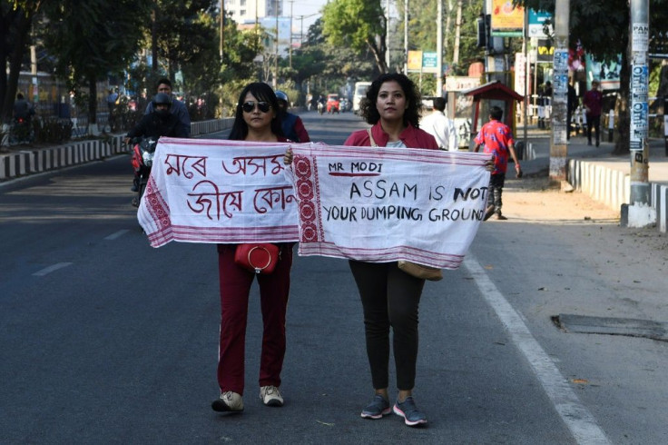 Two young women hold up their gamosas, emblazoned with "Mr Modi, Assam is not your dumping ground" in English and Assamese, the local official language