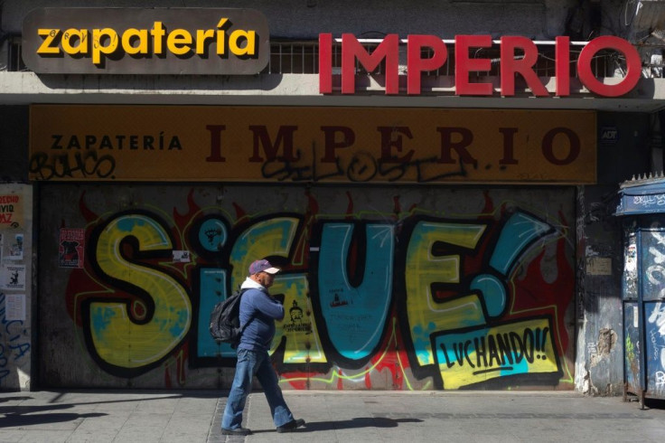 A man walks past a boarded up shoe store in valparaiso with graffiti that reads "Keep fighting!"