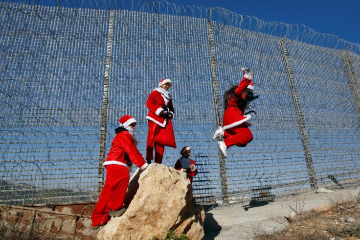 Palestinians in Father Christmas costumes jump off a rock by a barbed-wire section of Israel's controversial separation barrier near Wallajeh, west of Bethlehem in the occupied West Bank