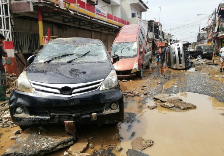 Residents walk by destroyed cars in Bekasi, West Java after flooding triggered by heavy rain hit the area