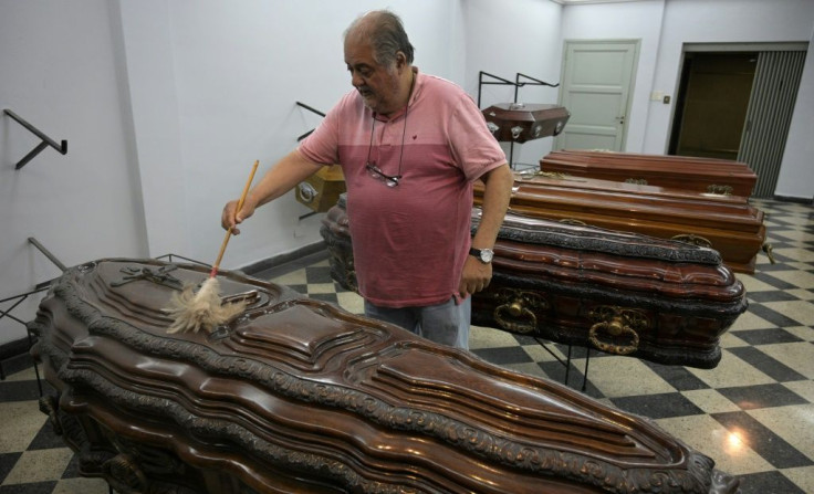 Eduardo Tapia uses a duster to clean coffins for sale in the Buenos Aires funeral home he owns, where he and his colleagues constantly are forced to lower their prices