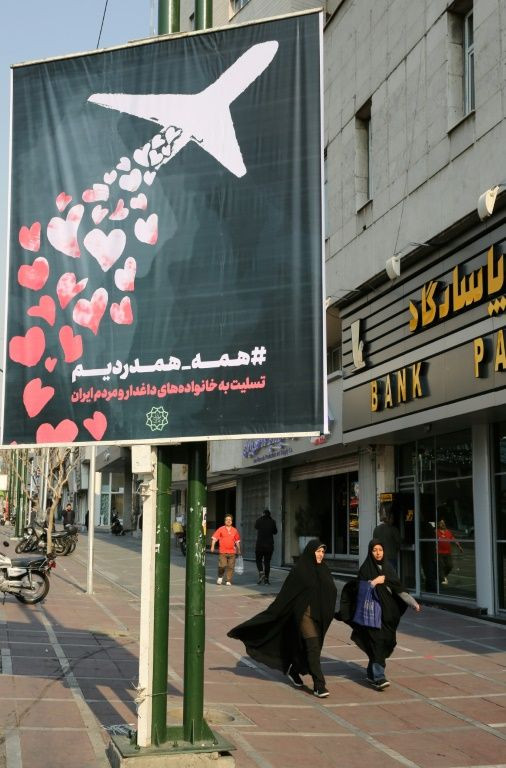Iranian women walk beneath a poster honouring the victims of a Ukrainian passenger jet accidentally shot down in the capital last week, in front of the Amirkabir University in the capital Tehran