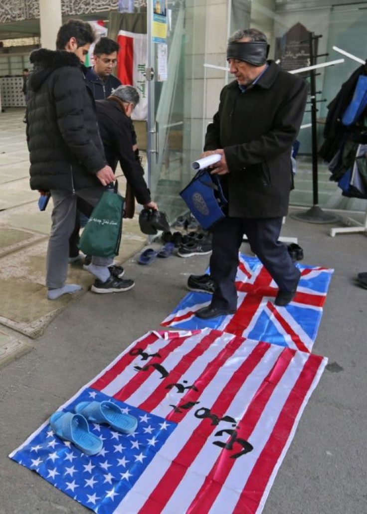 A supporter of the Basij, a militia loyal to the Islamic republic's establishment, walks over a Union Jack and US flag as he arrives at a memorial for victims of the Ukraine plane crash