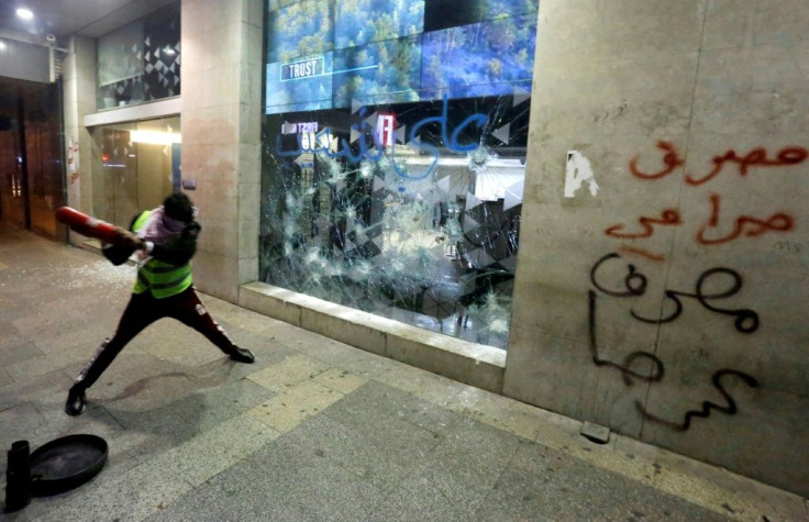 A Lebanese protester smashes the window of a bank in Beirut, with graffiti on the wall reading "banks are thieves", as demonstrators demand an end to a months-long political vacuum, with police firing tear gas at the start of a "week of wrath"