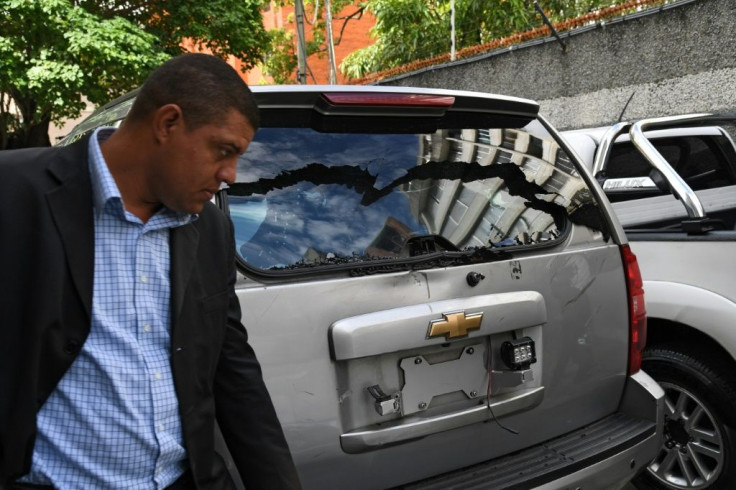 One of Juan Guaido's bodyguards walks next to a damaged vehicle after pro-government supporters allegedly attacked a convoy of opposition lawmakers