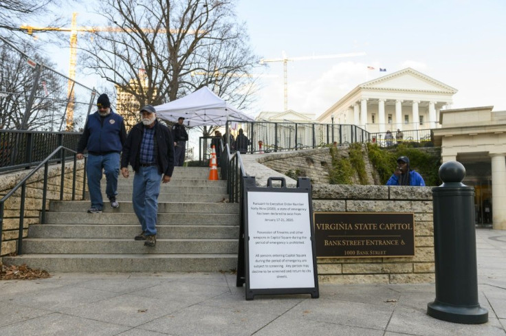 Visitors walk out of the grounds of Virginia's State Capitol in Richmond, near a sign advising that a state of emergency prohibits possession of firearms and other weapons in Capitol Square