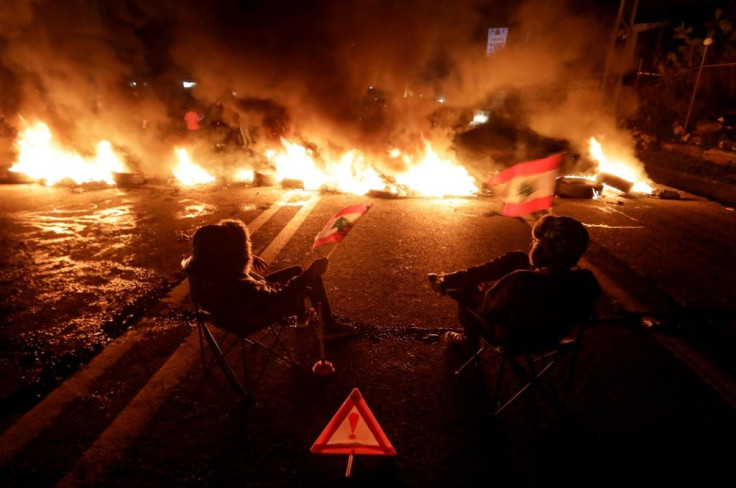 Anti-government protesters sit next to a section of the Beirut-Byblos highway