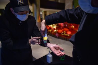 A hotel employee takes the temperature of a person that just arrived at the premise in Wuhan