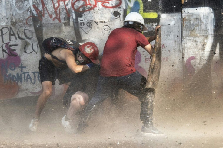 Demonstrators take cover as they clash with riot police during a protest against Chilean President Sebastian Pinera's government in Santiago, on January 17, 2020
