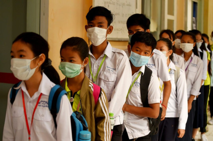 Masked Cambodian students line up to disinfect their hands with an alcohol solution before entering class at a school in Phnom Penh