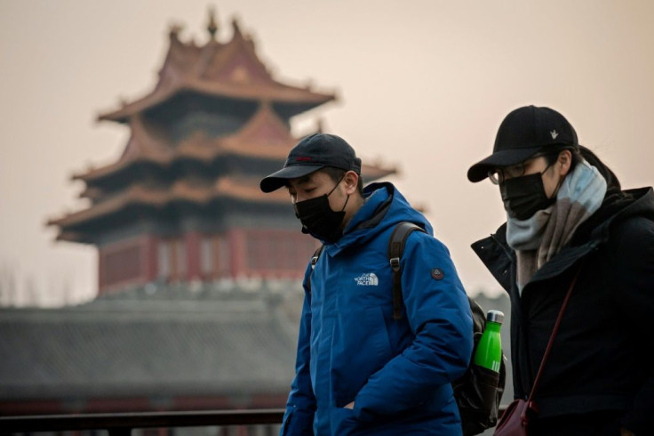 People wearing protective facemasks to help stop the spread of a deadly virus walk past the Forbidden City in Beijing