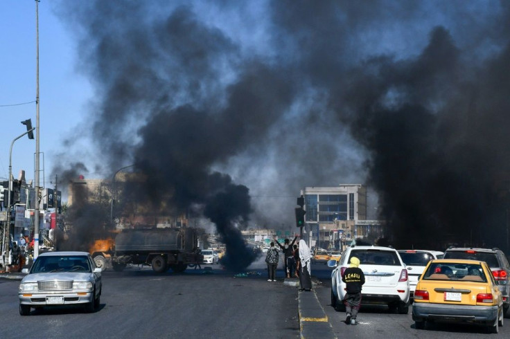 Iraqi anti-government demonstrators block a road with burning tires in the southern city of Nasiriyah during a demonstration against the new prime minister designate Allawi