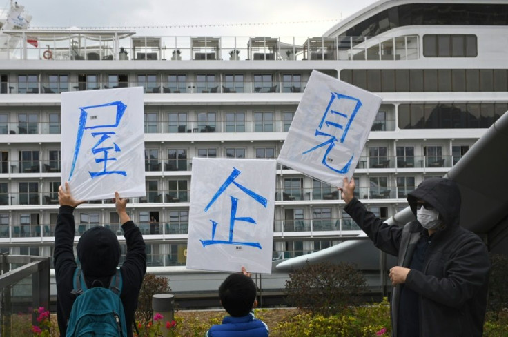 People on shore hold up placards that read "See you at home" for passengers on the World Dream cruise ship