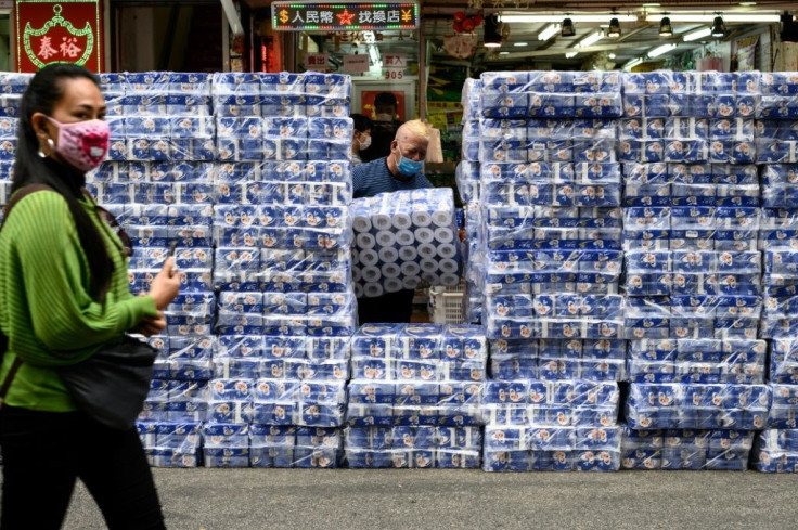 A woman wearing a protective face mask walks past stacks of toilet paper for sale in the Tsuen Wan district of Hong Kong