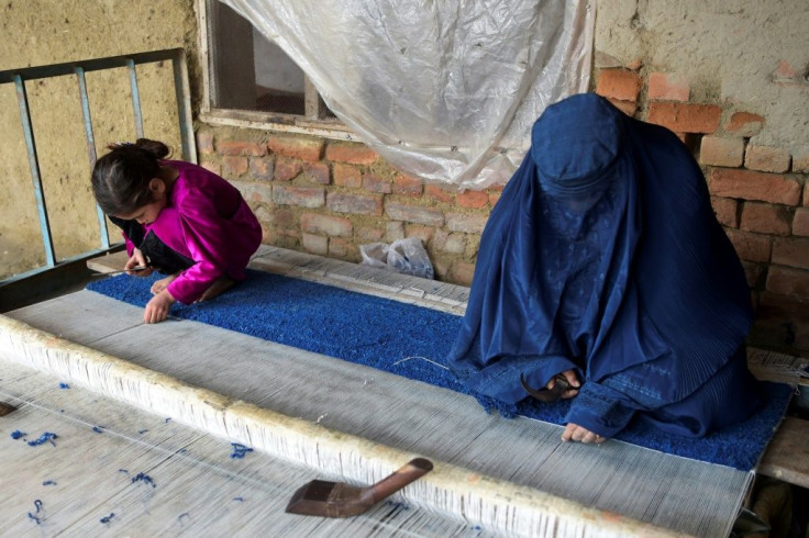 An Afghan refugee woman and her daughter make carpet at her home in a refugee camp in Peshawar