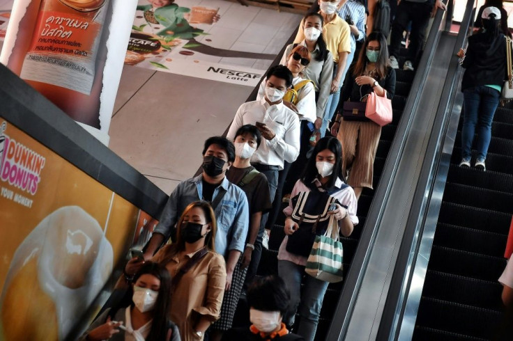 People wearing protective face masks ride down an escaltor during the morning commute in Bangkok