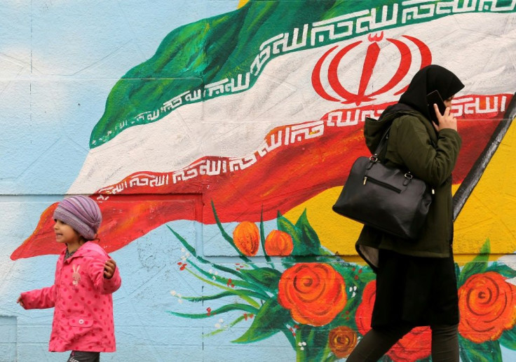A woman and child walk past a mural with the Iranian national flag in Tehran