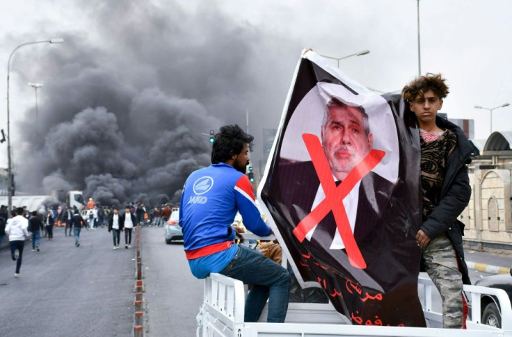 Iraqi demonstrators carry a poster of former premier-designate Mohammad Allawi covered with a red 'x' during an anti-government protest in Nasiriyah, on February 16