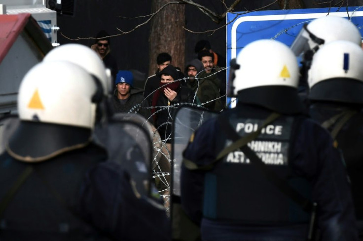 Greek riot police officers watch migrants acrss the barbed wire border