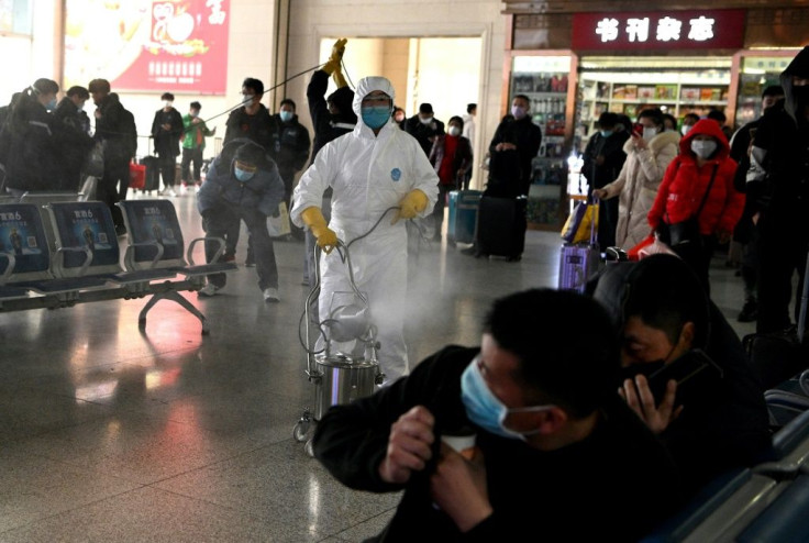 Passengers react as a worker wearing a protective suit disinfects the departure area of the railway station in Hefei, China