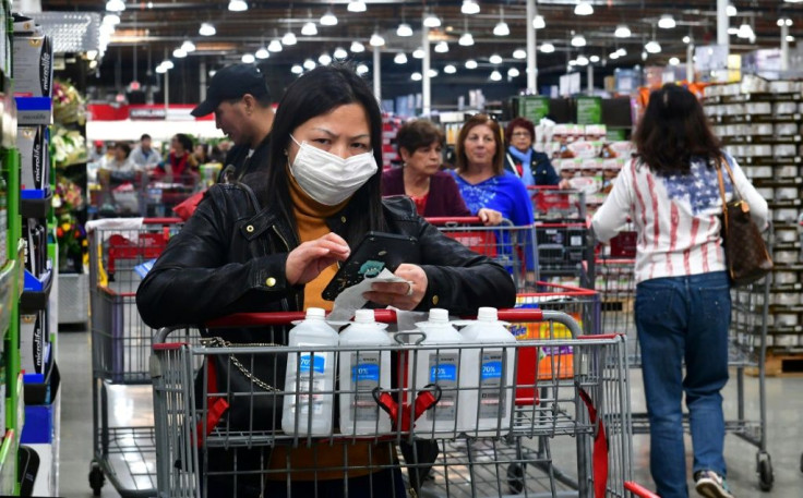 A woman wears a face mask while purchasing bottles of rubbing alcohol at a Costco store in California: while panic buying empties shelves, some economists fear a slump in consumer spending on the back of virus fears could hurt the economy