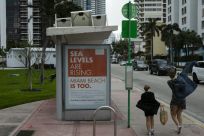 People walk past a billboard in Miami Beach discussing sea level rise: dozens of trucks have started dumping hundreds of thousands of tons of sand on Miami Beach as part of US government measures to protect Florida's tourist destinations against the effec