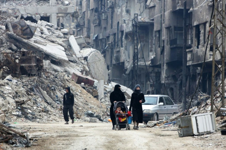 Syrian civilians walk thorugh the former rebel-held town of Harasta in Eastern Ghouta on March 30, 2018, a week after regime forces retook the town