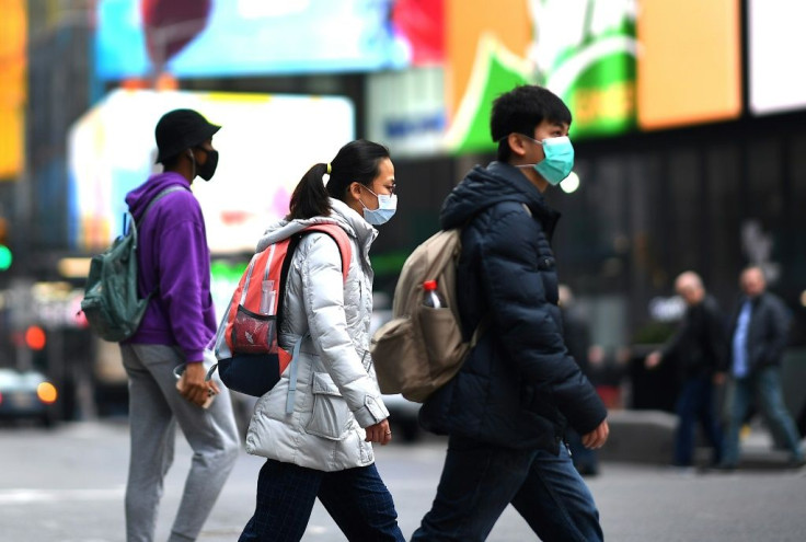 Tourists with masks walk through Times Square, which is emptying as New York state bans events with large crowds including Broadway shows