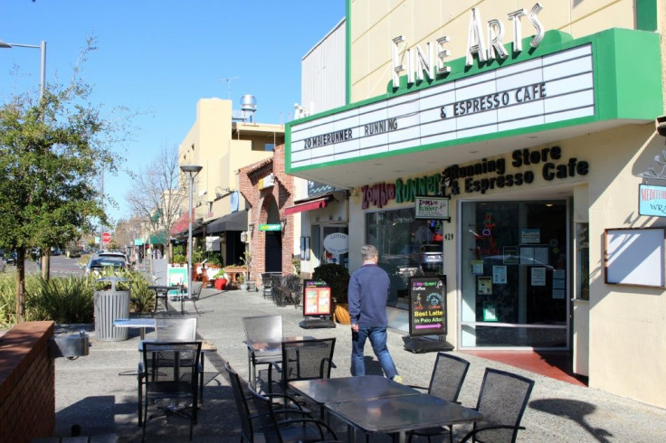 A man glances into ZombieRunner coffee shop as he strides along a quiet sidewalk in downtown Palo Alto, which is largely deserted due to people staying home over coronavirus caution