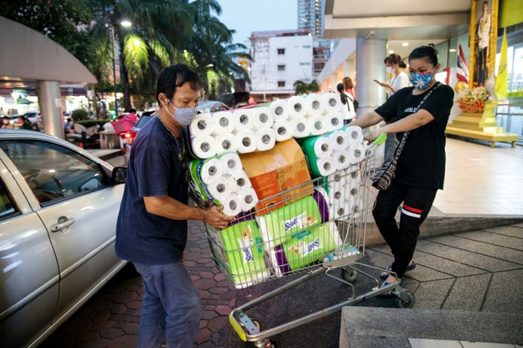 People wearing face masks amid concerns over the COVID-19 coronavirus push a shopping cart full of toilet paper and kitchen rolls at a supermarket in Bangkok on March 16, 2020