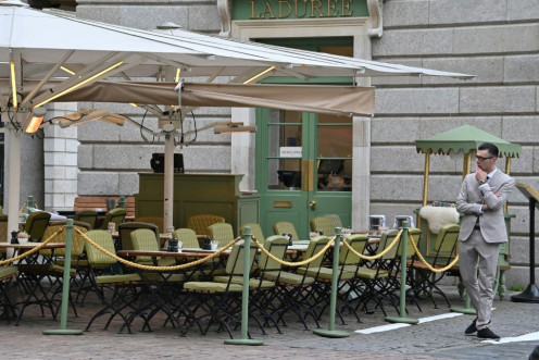 A restaurant employee stands by empty tables in a quiet Covent Garden in central London on March 17, 2020 after the UK government announced stringent social distancing advice