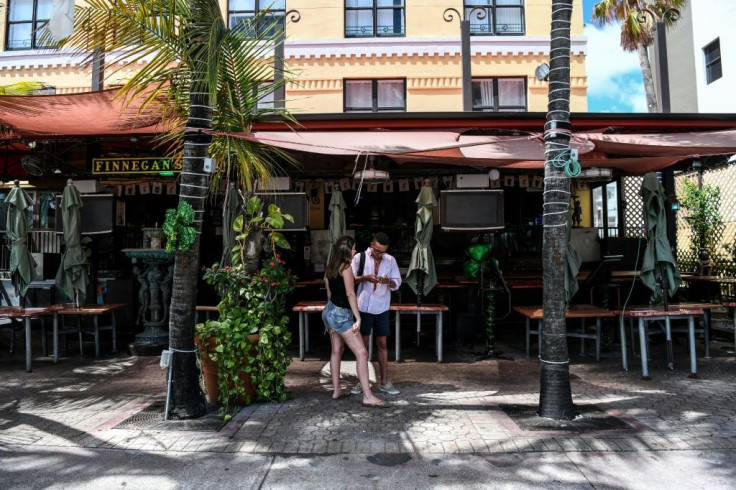 Standing in front of a closed restaurant, tourists check their phone for places still open on Ocean Drive in Miami Beach, Florida, after authorities ordered bars and restaurants to close as a precaution against the coronavirus pandemic