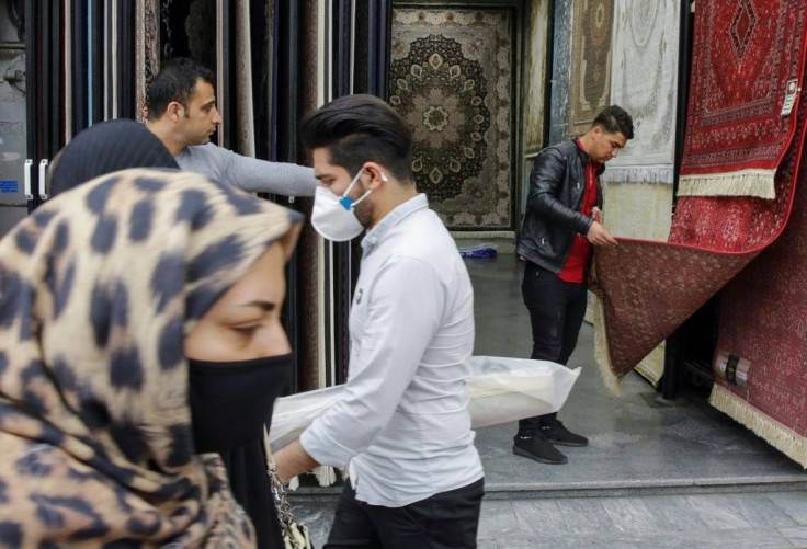 Iranians, some wearing protective masks, pass a carpet shop in the capital Tehran's grand bazaar