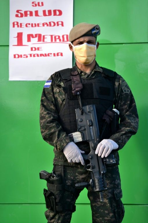 A Honduran presidential guard soldier wears a face mask and gloves as he stands next to a sign reading âFor your health, 1 meter distanceâ outside a supermarket in Tegucigalpa, on March 19, 2020