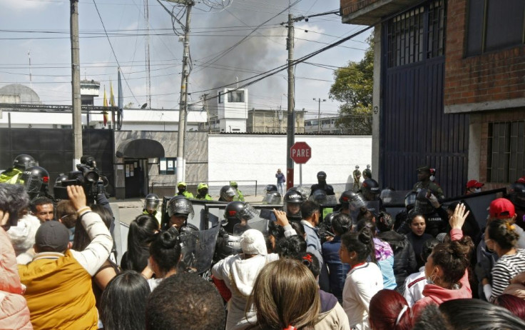 Relatives of inmates, journalists and riot police gather as smoke rises from the Modelo prison in Bogota following a riot that killed 23 prisoners, on March 22, 2020