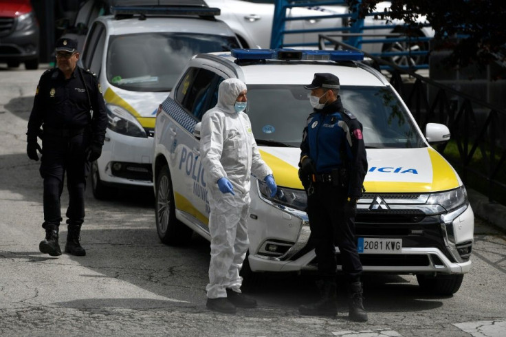 A policeman talks to a member of the Spanish Army's Military Emergency Unit (UME) wearing a protective suit outside the Palacio de Hielo shopping mall where an ice rink was turned into a temporary morgue on March 24, 2020 in Madrid